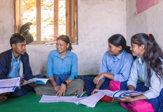 Five students sitting in a classroom with books.