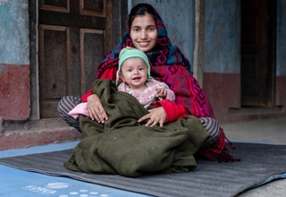 A mother holds her child outside their rented accommodation in Rukum West. 