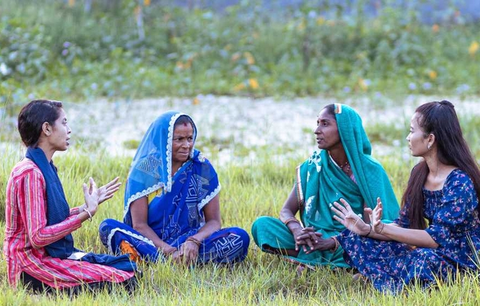 Four women gather in a grass field and talk