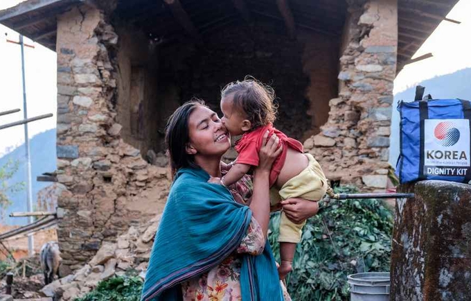 A mother holds her child outside their earthquake affected house in Jajarkot. 