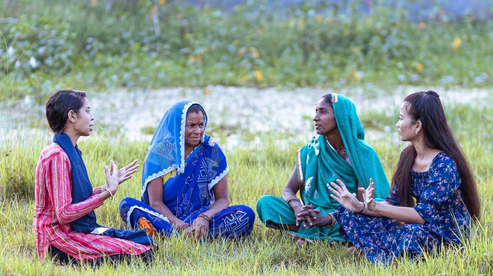 Four women gather in a grass field and talk