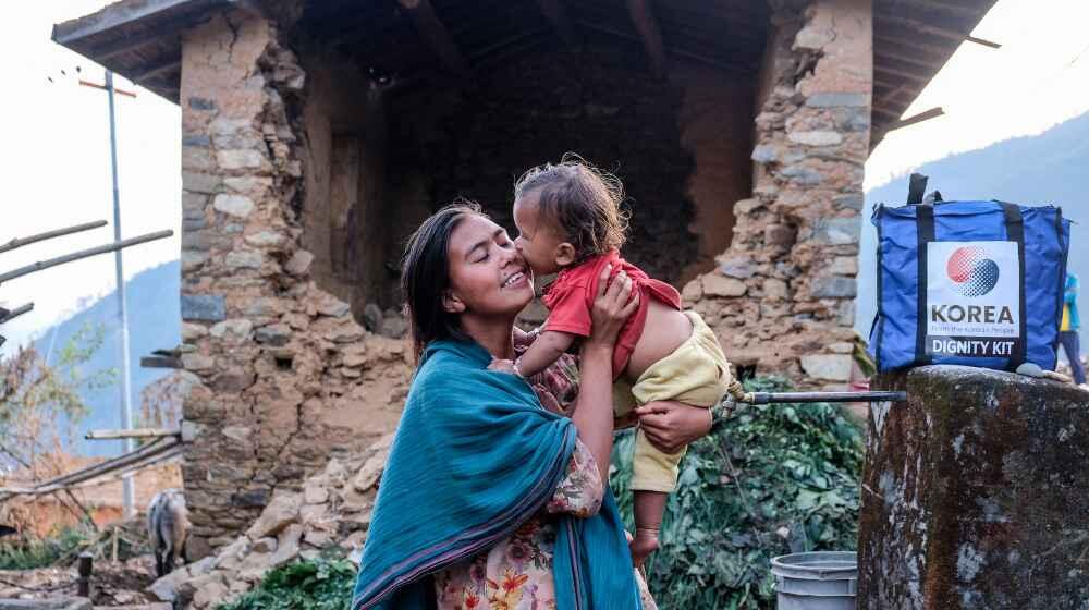 A mother holds her child outside their earthquake affected house in Jajarkot. 