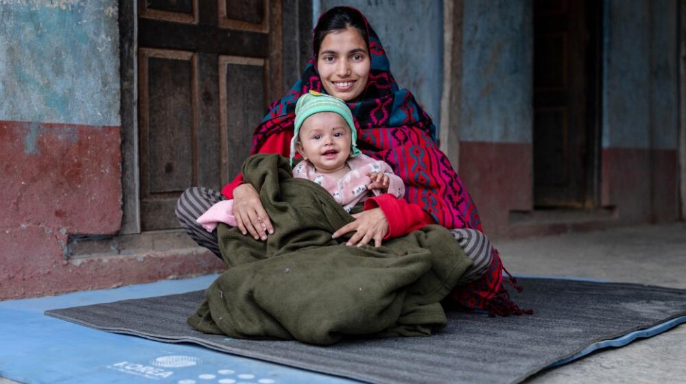 A mother holds her child outside their rented accommodation in Rukum West. 